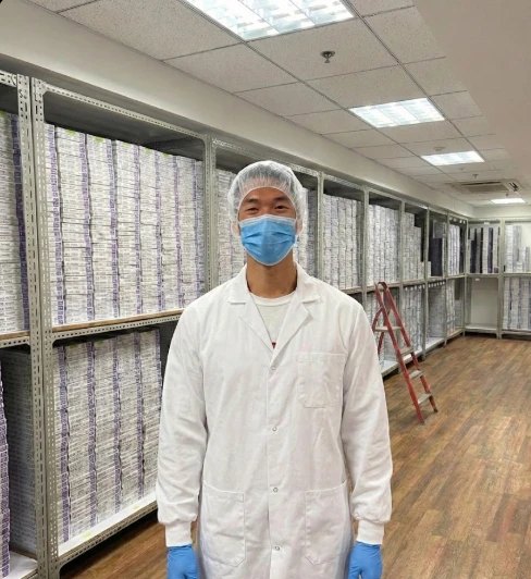 David in a lab coat and hairnet among shelves of product at his family’s silicone plant